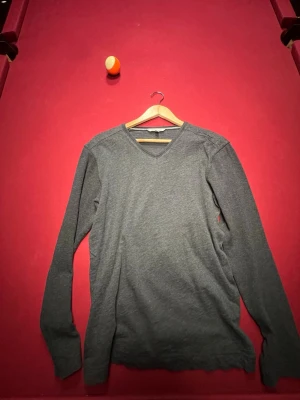 Mörkgrå V-ringad tröja Calvin Klein - Mörkgrå långärmad tröja från Calvin Klein Jeans med V-ringning. Enkel och stilren design, perfekt för lager-på-lager. Mjuk och skön bomullsblandning som passar till många olika outfits.