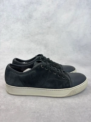 Svarta låga Lanvin sneakers i mocka - Stilrena svarta sneakers med ovandel i mocka och tåparti i slätt läder. Skorna har vita sulor och svarta skosnören för en clean look. Perfekta för dig som gillar minimalistisk stil och vill ha något som funkar till det mesta.