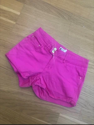 Rosa jeansshorts från Gina Tricot - Snygga rosa jeansshorts från Gina Tricot med klassisk femficksmodell och knappgylf. Shortsen har en tight passform och är tillverkade i ett mjukt bomullsmaterial med lite stretch. Perfekta för sommaren och ger en färgstark look.