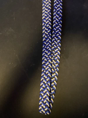 Randigt flätat bälte i blått och vitt - Snyggt flätat bälte med randigt mönster i blått, vitt och svart. Bältet har en flexibel design och passar perfekt till jeans eller chinos för en cool och avslappnad stil.