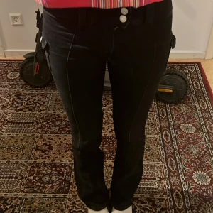 Svarta cargopants med bootcut - Säljer ett par jättefina svarta  bootcut och låg midjade jeans. Byxorna har fickor med knapp på sidorna och två knappar i midjan. Säljer pga att de blivit lite för små för mig🩷💕