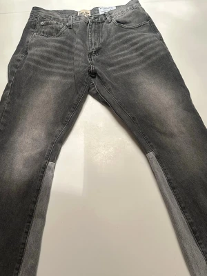 Gråa bootcut jeans med rå kant - Säljer ett par gråa bootcut jeans från Calvin Klein med cool tvätt och slitna, råa kanter nertill. Jeansen har fem fickor, hög midja och kontrasterande paneler längs benen för en unik look. Perfekta för dig som vill sticka ut med din stil.