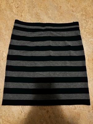 Randig svart och grå kortkjol - Snygg kortkjol med breda svarta och gråa horisontella ränder. Kjolen har en rak passform och är tillverkad i mjukt bomullsmaterial. Perfekt för en avslappnad och trendig look. Pris kan diskuteras💖