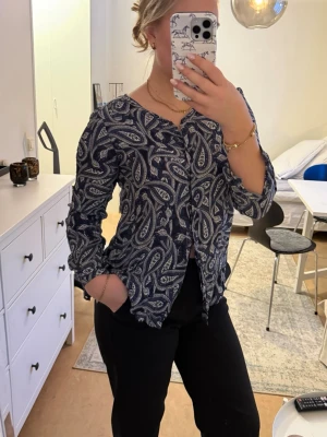 Massimo Dutti blus - Säljer en blå blus med vitt paisleymönster och v-ringning. Blusen har lång ärm och lätt vågiga kanter vid ärmslut och nederkant. Perfekt för dig som gillar unika mönster och en avslappnad men snygg stil.