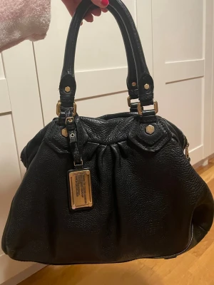Svart Marc Jacobs handväska  - Svart marc jacobs väska!! Köpt på second hand och väl använd. I bra skick, men har en del skavanker, som syns på bilderna. Slitningar vid handtagen, tuschsträck inuti väskan som jag ej försökt få bort, färg som tappats på metallen, och slitage i lädret vid dragkedjan. Därav det nedsatta priset !❤️fråga gärna om fler bilder!!! 