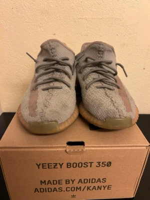 Adidas Yeezy Boost 350 V2  - Säljer ett par Yeezy Boost 350 V2 i färgen True Form. Skorna har en stickad ovandel i grått med orange detaljer och genomskinlig sula i gummi. Ikonisk siluett med bekväm Boost-dämpning och klassiska Yeezy-detaljer. Perfekta för dig som gillar streetwear.