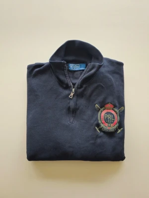 Mörkblå quarter zip från Polo Ralph Lauren - Polo Ralph Lauren quarter zip - crest / PRL LXVII - Polo Winter Challenge Cup - Mercer Club  Perfkt för någon som letar efter vintage-känsla.  Storlek: XXL  Färg: mörkblå / marinblå  Skick: Bra begagnat skick. Lätt nopig på ett litet ställe samt ytterst lätt blekt på något parti. Kanske krympt något. Väldigt bra skick för att vara så gammal!   Tillverkad ca 2008-2012 tror jag.