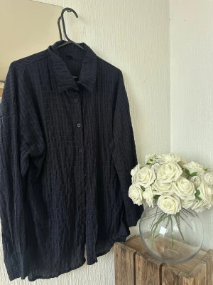 Mörkblå rutmönstrad skjorta - Mörk blå skjorta med diskret rutmönster och klassisk krage. Skjortan har knäppning framtill och långa ärmar. Perfekt för en stilren look och lätt att matcha med andra plagg.