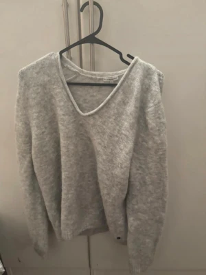 Ljusgrå stickad tröja med v-ringning - Mysig ljusgrå stickad tröja med djup v-ringning och långa ärmar. Tröjan har en avslappnad passform och ribbade muddar vid ärmslut och nederkant. Perfekt för lager på lager och enkel att matcha med olika outfits. För mer bilder/justering av pris skriv gärna❤️🤗