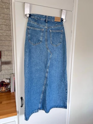 Lång blå jeanskjol med slits från Carin Wester, storlek 34 (nyskick) - Lång blå jeanskjol från Carin Wester med hög midja och slits framtill. Rak passform och  gjord i kraftig denim. 100% bomull. Använd en gång - nyskick. Finns fler bilder!