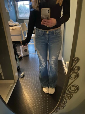Ljusblå bootcut jeans med slitningar - Säljer ett par ljusblå bootcut jeans från Gina 14+ med slitningar. Jeansen har låg midja och snygga detaljer på bakfickorna. 