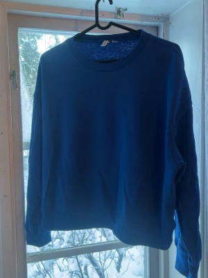 Blå sweatshirt utan huva - En enkel och stilren blå sweatshirt med rund halsringning och långa ärmar. Tröjan har en avslappnad passform och är tillverkad i ett mjukt material, perfekt för en casual look. Inga synliga loggor eller tryck.