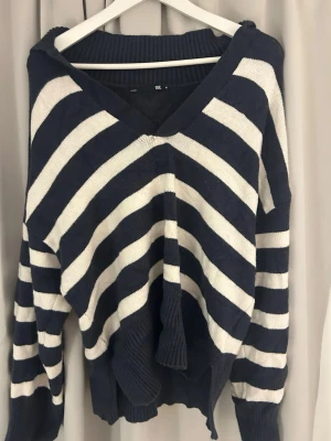 Randig stickad tröja med V-ringning - Mysig stickad tröja med breda marinblå och vita ränder. Perfekt för lager-på-lager och chill stil. Materialet känns mjukt och stretchigt. Kan kännas större än storleken som står