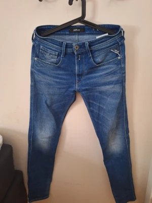 Blå Replay Anbass jeans herr - Snygga blå jeans från Replay, modell Anbass. De har en smal passform, klassisk femficksdesign och coola slitningar på låren. Perfekta för dig som gillar en modern och avslappnad stil. Jeans i stretchigt denim för extra komfort.
