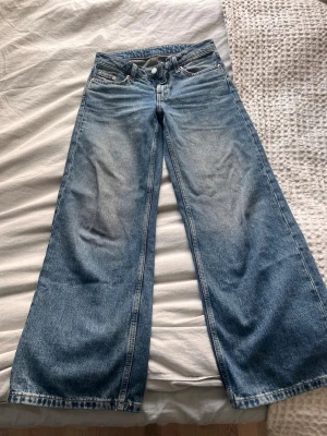 Blåa wide leg jeans från Weekday - Säljer ett par blåa wide leg jeans från Weekday med hög midja och klassisk femficksdesign. Jeansen har en snygg tvättad look och är tillverkade i kraftig denim. Perfekta för dig som gillar en avslappnad och trendig stil.