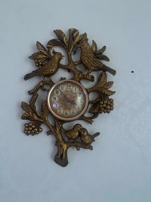 Vintage väggklocka med fåglar - Unik väggklocka från Junghans med detaljerade fåglar och grenar i guldtonad metall. Klockan har klassiska siffror och ett dekorativt urtavla. Drivs med AA-batteri och har en tydlig retrostil som sticker ut på väggen.