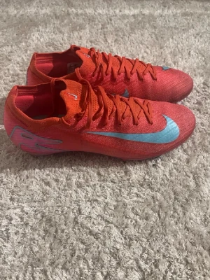 Nike Mercurial vapor 16 röda fotbollsskor - Säljer ett par Nike Mercurial vapor 16 fotbollsskor i en riktigt snygg röd färg med ljusblåa detaljer och swoosh. Skorna har en strömlinjeformad design, tunn ovandel i syntetmaterial och klassisk snörning. Perfekta för dig som vill ha speed och kontroll på planen.