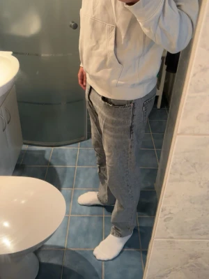 Grå tvättade raka jeans - Säljer ett par grå tvättade jeans med rak passform och klassisk femficksdesign. Jeansen har hög midja och avslappnad look, perfekta för en chill och trendig stil. Materialet är denim i bomull och färgen är ljusgrå med tvättade detaljer. Storlek W31, L32