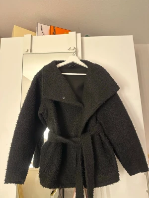 Svart teddyjacka med bälte - Mysig svart teddyjacka ifrån Gina Tricot med bred krage och knytbälte i midjan. Jackan har en oversized passform och är gjord i fluffigt teddy-material som ger en trendig look. Perfekt för vår/höst väder!