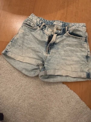 Ljusblå denimshorts från Lindex - Säljer ett par ljusblå denimshorts från Lindex med upprullade benslut och klassisk femficksdesign. Shortsen har bälteshällor och knappgylf. Perfekta för varma dagar och ger en avslappnad look. Jag brukar vika ner dem i midjan så blir de low waist och skitsnygga! Skulle säga att de passar en xxs eller xs. Skitsnygg färg till sommaren!