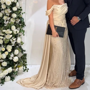 Champagnefärgad klänning  - Superfin champagnefärgad långklänning med offshoulder och släp. Använd 1 gång och köptes för 2,8 hos lamoda dress. Den har en korsettknytning vid ryggen så man kan skjustera och spänna hur tajt man vill ha det. Passar någon som är storlek 38/40. 