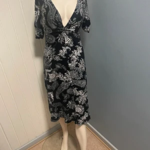 Två mönstrade klänningar med v-ringning - Säljer fem snygga klänningar med v-ringning. Ena klänningen är svart med vitt paisleymönster och har kort ärm, den andra har färgglatt orientaliskt mönster i rosa, blått och grönt. Båda är knälånga och har en avslappnad passform.