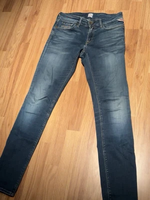 Blå jeans från replay, liknande passform som Anbass. - Snygga blå jeans från Replay med klassisk femficksdesign och slitna detaljer. Jeansen har en låg midja, dragkedjegylf och kontrastsömmar. Perfekta för en avslappnad och trendig look.