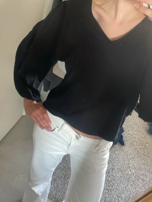 Svart blus med v-ringning och puffärm - Säljer en svart blus med v-ringning och långa puffärmar. Blusen har en lös passform och är tillverkad i ett lätt, strukturerat tyg som ger en avslappnad men ändå stilren look. Perfekt att matcha med både jeans och kjol.