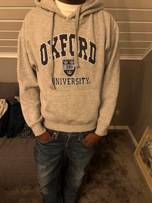 Grå Oxford University hoodie - Snygg grå hoodie med Oxford tryck | Storlek: S | Längd på han som bär tröjan: 178cm | Man ser även att piggen på ena stnöret har gått upp| Hör av er för frågor😁