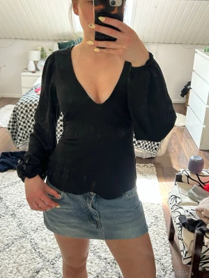 Svart v-ringad blus med puffärm - Snygg svart blus med djup v-ringning och långa puffärmar. Modellen är figurnära i midjan och har lätt utsvängd nederkant. Perfekt för dig som gillar en enkel men trendig look.