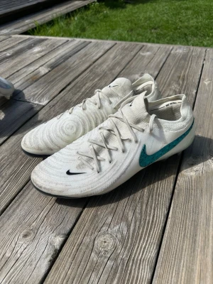 Nike Phantom GX 2 LV8 Elite FG - Vit/Emerald - Säljer ett par Nike Phantom GX 2 Elite som tyvärr var för stora för mig. Hann användas 2 gånger på gräsplan. Lite lätt leriga/missfärgade men har inga skråmor över huvudtaget. Original pris är 2899kr och jag säljer de för 999kr efter 2 gånger användning. Storlek 45 EU. Det är FG underlag. Skriv vid intresse, fler bilder eller någon fundering. Priset är fast!