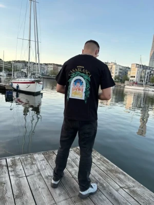 Svart Casablanca t-shirt med tryck - Svart t-shirt från Casablanca med färgglatt tryck på ryggen och mindre tryck på bröstet. Klassisk passform med korta ärmar och rund hals. Perfekt för dig som vill sticka ut med en snygg och trendig look.