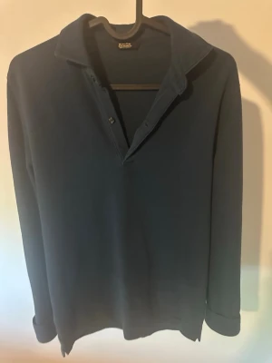 Mörkblå långärmad piké från Massimo Dutti - Mörkblå långärmad piké från Massimo Dutti med klassisk krage och knappslå. Tröjan har en stilren och enkel design som passar perfekt till jeans eller chinos. Tillverkad i mjukt material för en bekväm känsla hela dagen.