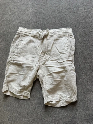 Beiga linneshorts Kappahl  - Snygga beiga shorts i linne med avslappnad passform och snörning i midjan. Shortsen har sidofickor och en bakficka med knapp. Perfekta för varma dagar och enkel att matcha med t-shirt eller skjorta. Nice till sommaren. (pris kan diskuteras)