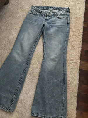 Ljusblå bootcut jeans - Säljer ett par ljusblå bootcut jeans med klassisk femficksdesign och låg midja. Jeansen har en lätt tvättad look och vida ben nedtill. Perfekta för dig som gillar en avslappnad och retro stil. Använt 2 gånger 