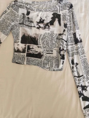 Svartvit croppad långärmad topp - Trendig croppad topp med lång ärm i svartvitt tidningsmönster. Tunt och stretchigt material som sitter tajt mot kroppen. Perfekt för dig som gillar unika prints och vill sticka ut.