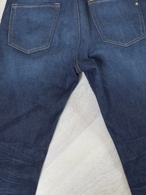 Mörkblå jeans från Replay - Snygga mörkblå jeans från Replay med klassisk femficksdesign och kontrastsömmar. Jeansen har raka ben och är tillverkade i ett slitstarkt denimtyg. Perfekta för dig som gillar en tidlös och stilren look.