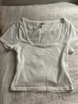 Vit topp Nelly - Vit kortärmad topp från Nelly med snygg fyrkantig ringning. T-shirten är i mjuk bomull och har en figurnära passform som passar perfekt till jeans eller kjol. Enkel och stilren design som är lätt att matcha.