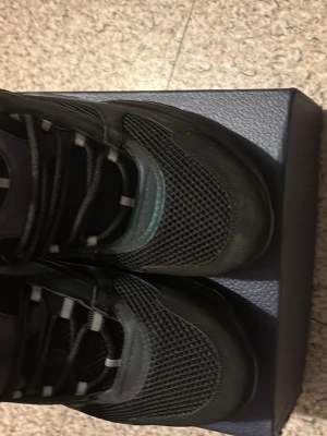 Svarta sneakers med reflexdetaljer - Svarta sneakers med mesh- och syntetmaterial, coola reflekterande detaljer i turkos och lila samt svarta snören. Skorna har en sportig vibe och låg profil, perfekt för dig som gillar streetstyle och vill sticka ut lite extra.