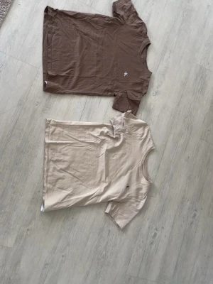 Två Ck t-shirts i brunt och beige - Säljer två stilrena Ck t-shirts i brunt och beige med liten broderad logga på bröstet. Båda har klassisk passform, rund hals och korta ärmar. Perfekta till jeans eller shorts för en clean look.