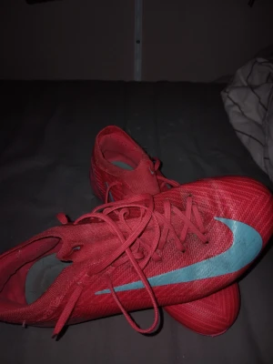 NIKE MERCURIAL PRO ROSA FOTBOLLSKOR - Säljer ett par Nike Mercurial fotbollsskor i en snygg rosa färg med ljusblå swoosh. Skorna har snörning och är tillverkade i syntetmaterial för bra grepp och lätt känsla på planen. Perfekta för dig som vill sticka ut på fotbollsplanen.