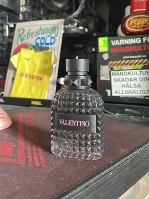 Valentino parfymflaska svart nitar - Snygg parfymflaska från Valentino i svart glas med nitar och strukturerad yta. Flaskan har en svart etikett med Valentino-loggan i vitt och ett stilrent svart lock. Perfekt för dig som gillar lyxiga och unika dofter. 25 ml kvar i den 