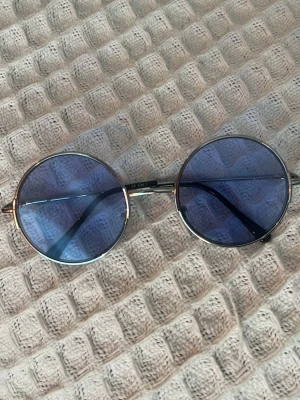 Runda solglasögon med blått glas - Säljer ett par stilrena runda solglasögon med tunna silverfärgade bågar och blåtonade glas. 