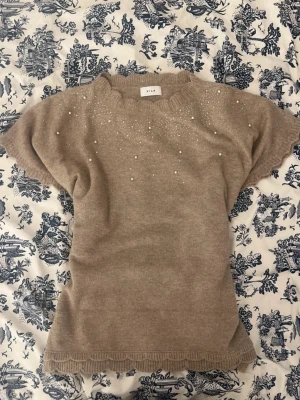 Beige stickad topp från Vila med fina pärl- och glitterdetaljer  - Mjuk och elegant modell med korta ärmar och feminin passform. Perfekt när man vill vara både bekväm och lite extra uppklädd 🌸Superfin till både jeans, kjol eller kostymbyxor. Passar lika bra till vardag som middag eller höstiga cafédejter ☕✨