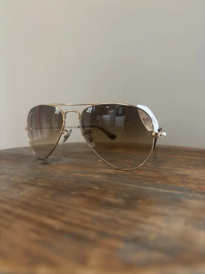 Ray-Ban Gradient aviator solglasögon guld - Snygga Ray-Ban aviator solglasögon med guldfärgad metallbåge och bruna tonade glas.stl S.  Klassisk pilotmodell som ger en cool vibe och passar perfekt till sommaren. Tunn båge och näskuddar för extra komfort.