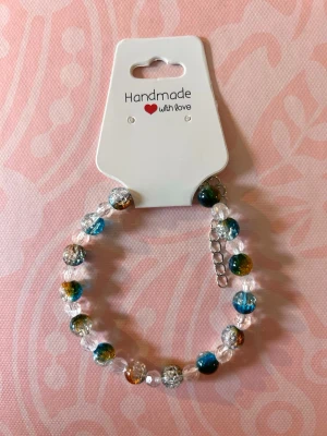 Färgglatt pärlarmband - Snyggt armband med pärlor i blått, grönt och orange mixat med transparenta glaspärlor. Armbandet har justerbar kedja och är handgjort, perfekt för att ge din stil en unik touch.