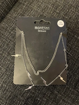 Silverfärgat halsband med blixtar Montini - Snyggt silverfärgat halsband från Montini med små blixtformade hängen längs kedjan. Halsbandet har en tunn kedja och coola detaljer som ger en trendig look. Perfekt accessoar för att lyfta din outfit med en edgy touch.