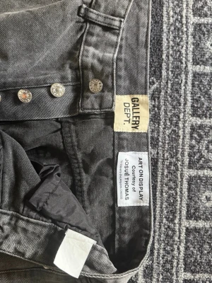 Svarta jeans från Gallery Dept. - Säljer ett par svarta jeans från Gallery Dept. med klassisk femficksmodell och knäppning med metallknappar. Jeansen har en tvättad look och raka ben. Märkesetikett på insidan och detaljerad design av Josué Thomas.