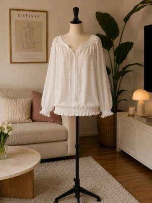 Vit romantisk blus med volangdetaljer - Luftig vit blus med långa ärmar, v-ringning och knytband framtill. Blusen har volangkant vid halsringning, ärmslut och nederkant samt smockdetaljer som ger en feminin touch. Perfekt för en trendig och avslappnad look.