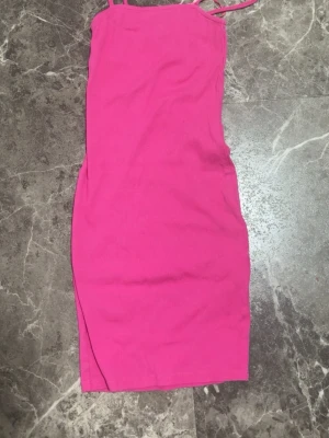 Rosa ribbad kort klänning - En snygg rosa ribbad klänning med smala axelband och tight passform. Klänningen är kort och har en enkel, stilren design som passar perfekt till sommaren. Materialet är stretchigt och bekvämt.